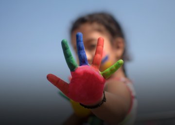 Imagem de criança desfocada com a mão direita, colorida, à frente do rosto