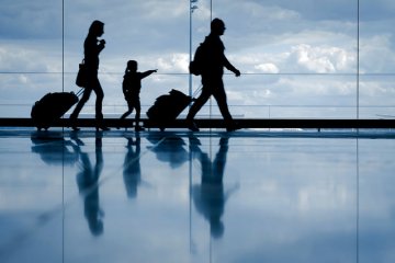 Imagem de dois adultos com malas e uma criança caminhando em aeroporto